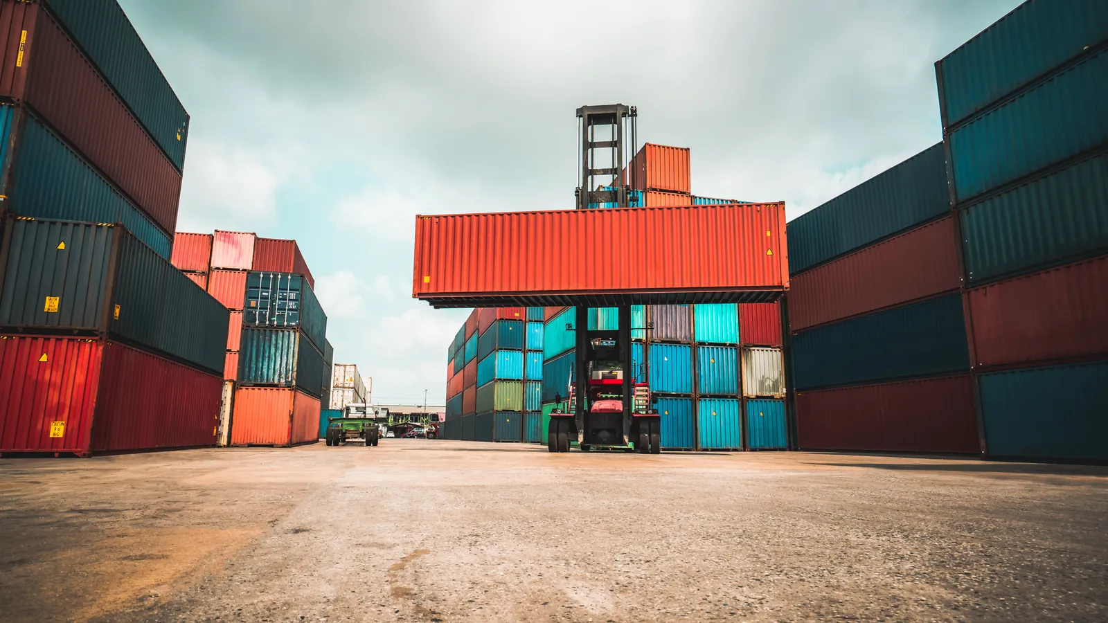 Shipping containers stacked in a logistics yard with a reach stacker